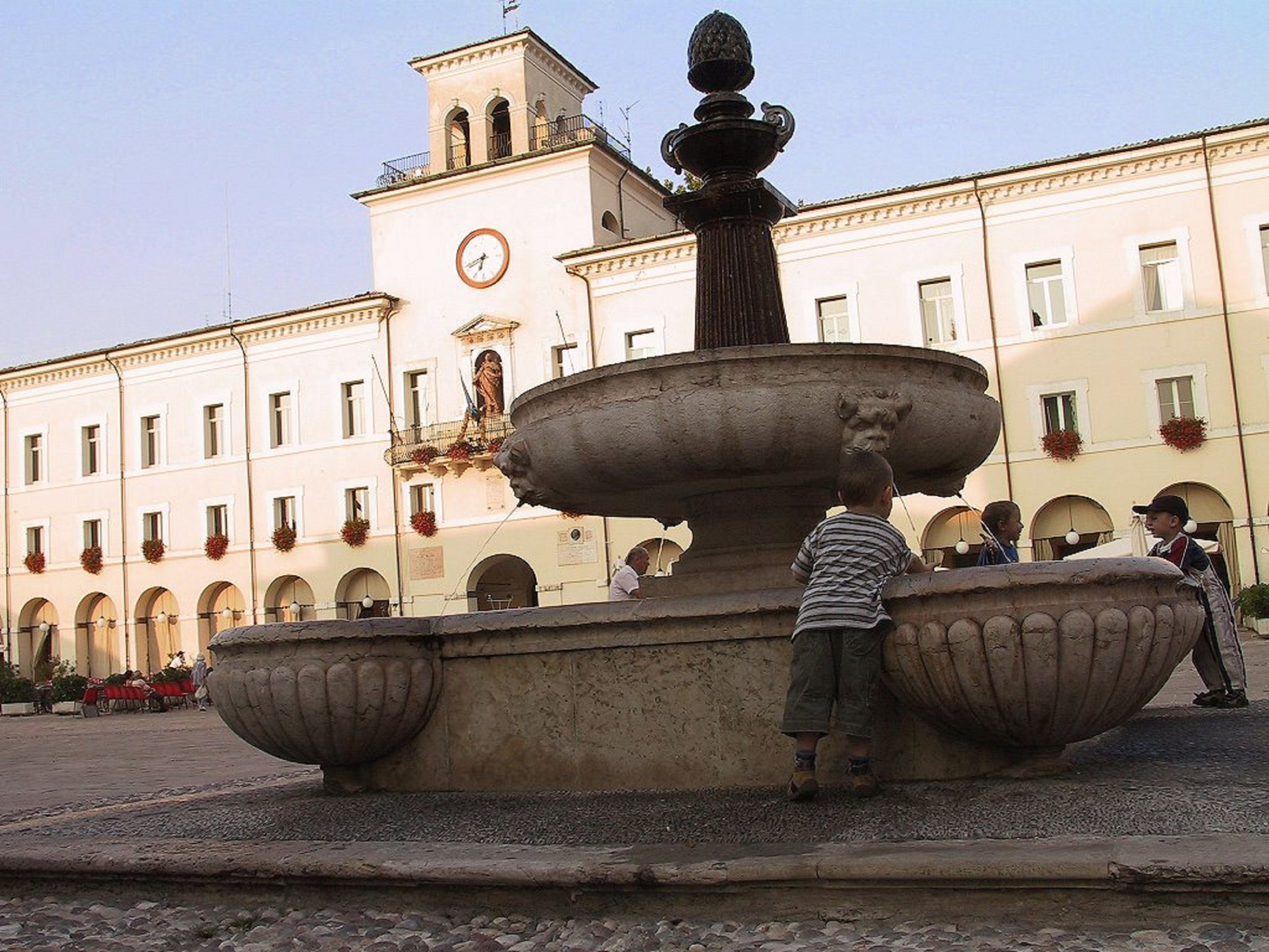 A fountain with a statue in the center, surrounded by a plaza with buildings in the background.