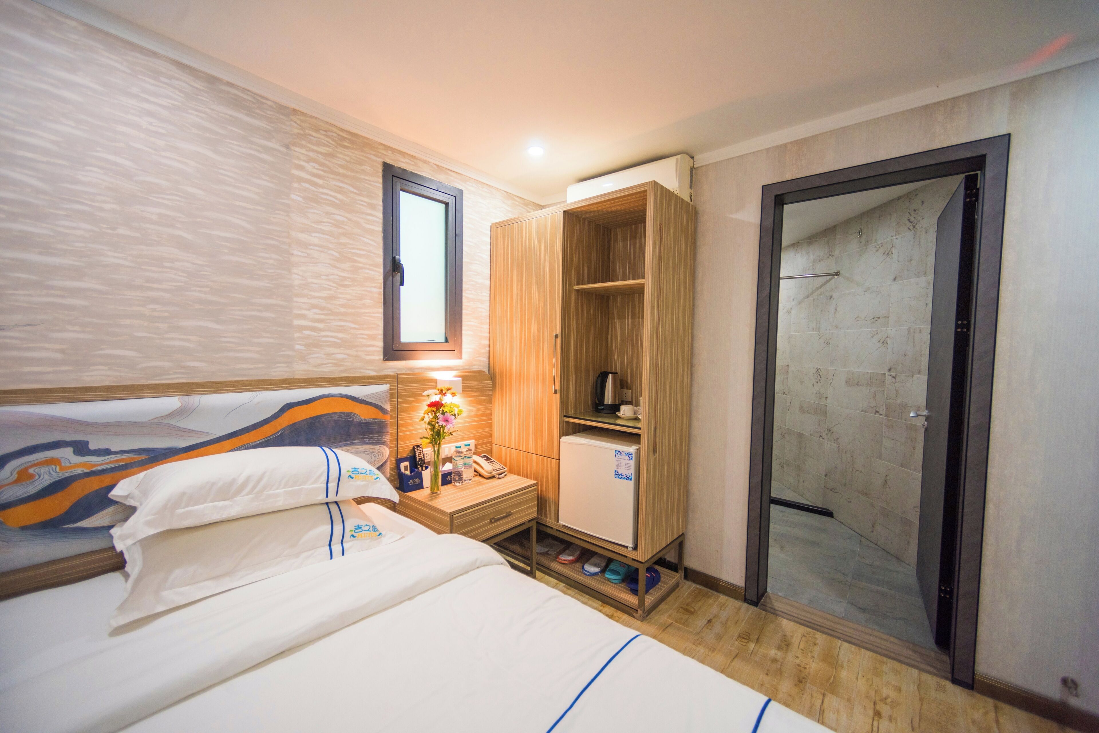 A hotel room with a bed, a nightstand, a minibar, a wardrobe, and a shower area.