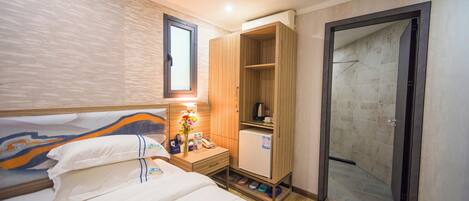 A hotel room with a bed, a nightstand, a minibar, a wardrobe, and a shower area.