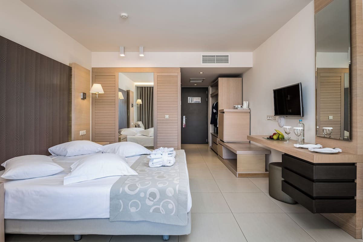 A modern hotel room with a bed, bedside tables, a desk with a TV, and a bathroom visible through an open door.