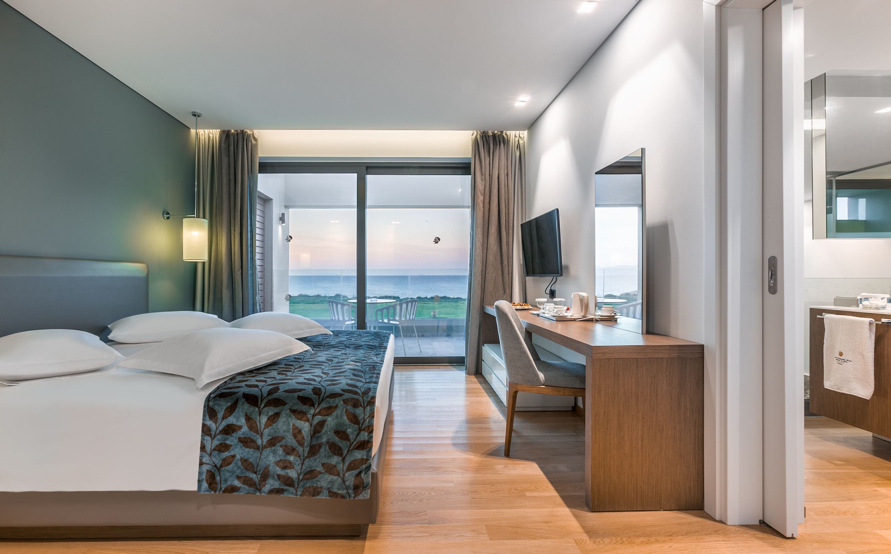 Een moderne hotelkamer met een bed, bureau en een groot raam met uitzicht op zee.