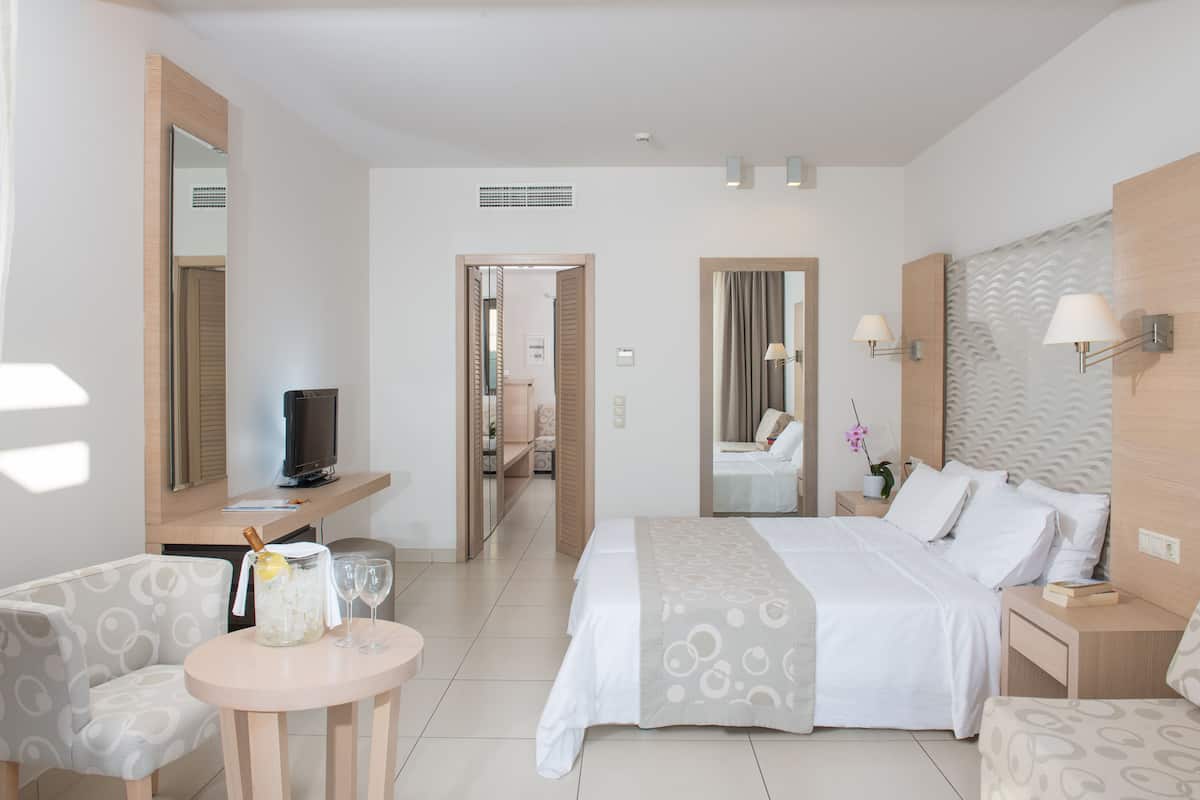 A hotel room with a bed, bedside tables, a TV, a seating area with a table and chairs, and a bathroom visible through an open door.