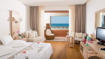 Habitación de hotel con balcón, cama, sofá, sillón, escritorio y televisión.