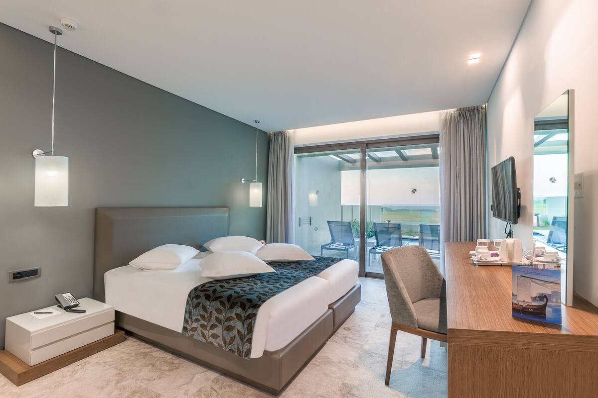 A modern hotel room with a large bed, a desk with a chair, a telephone, and a television.