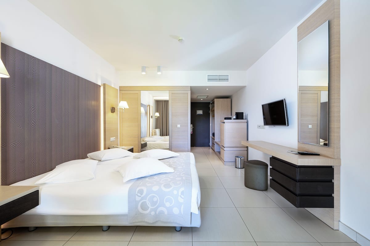 A modern hotel room with a large bed, a desk, a television, and a mirror.