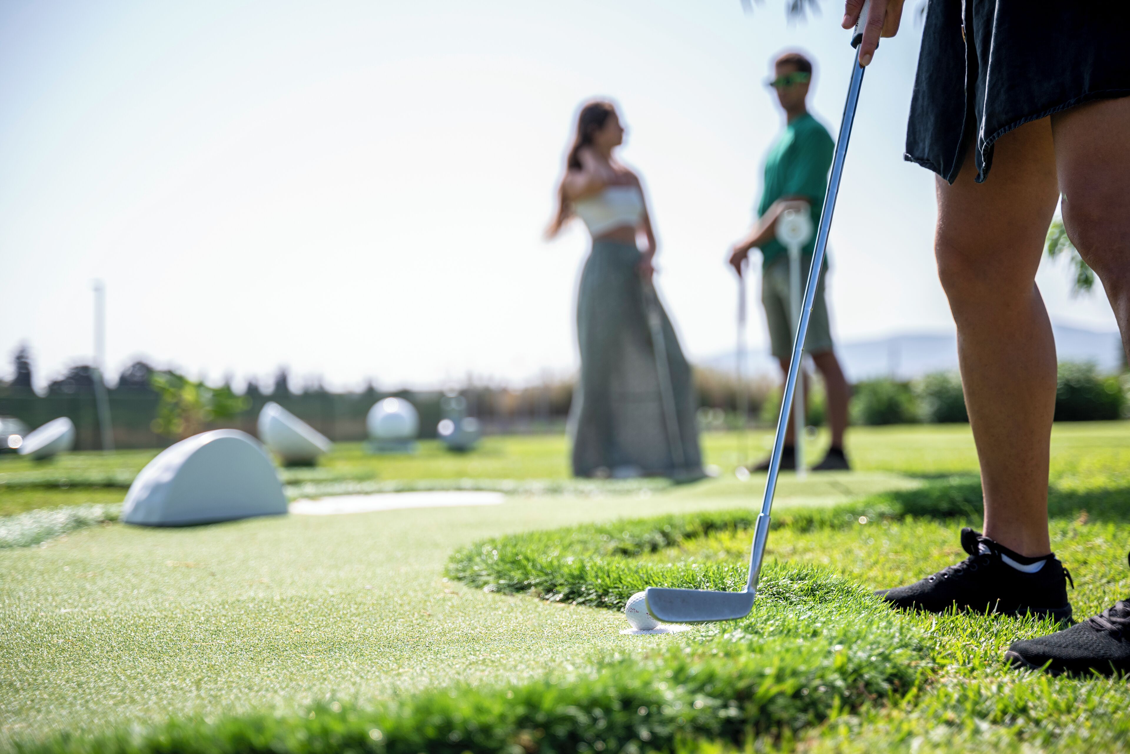 A golf course with a putting green, a sand bunker, and a flagstick.