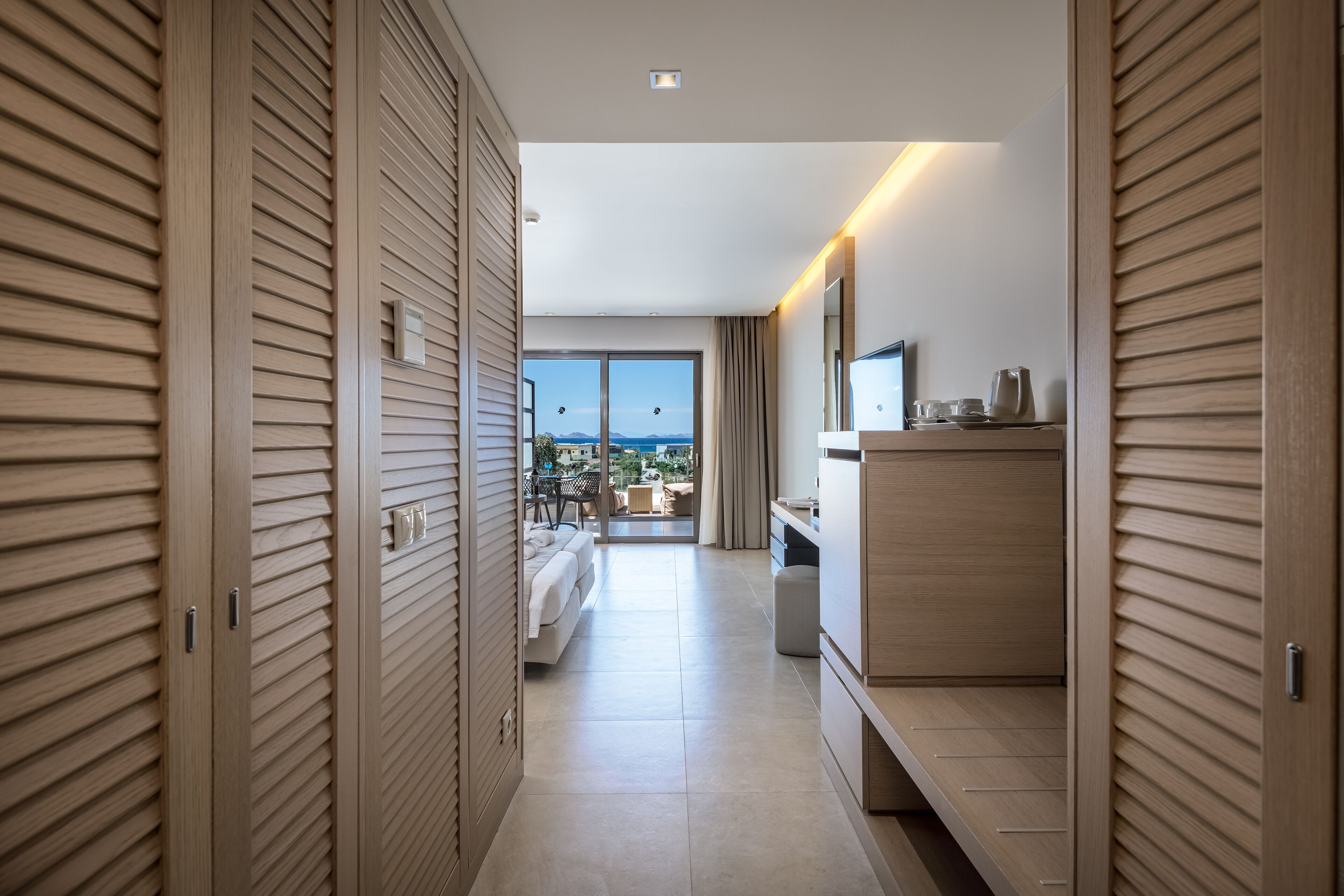 A hotel room with a balcony, a bed, a desk, and a wardrobe.