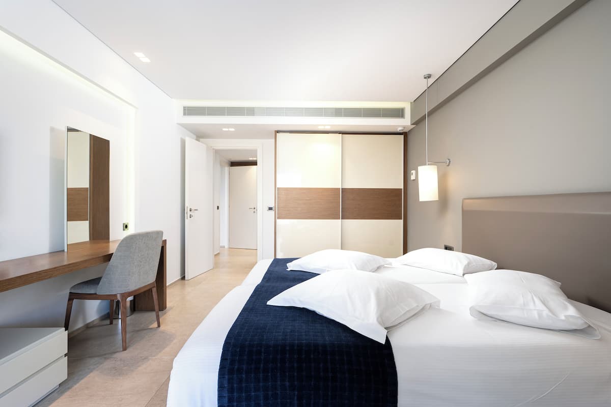 A modern hotel room with a bed, a desk, a chair, and a wardrobe.