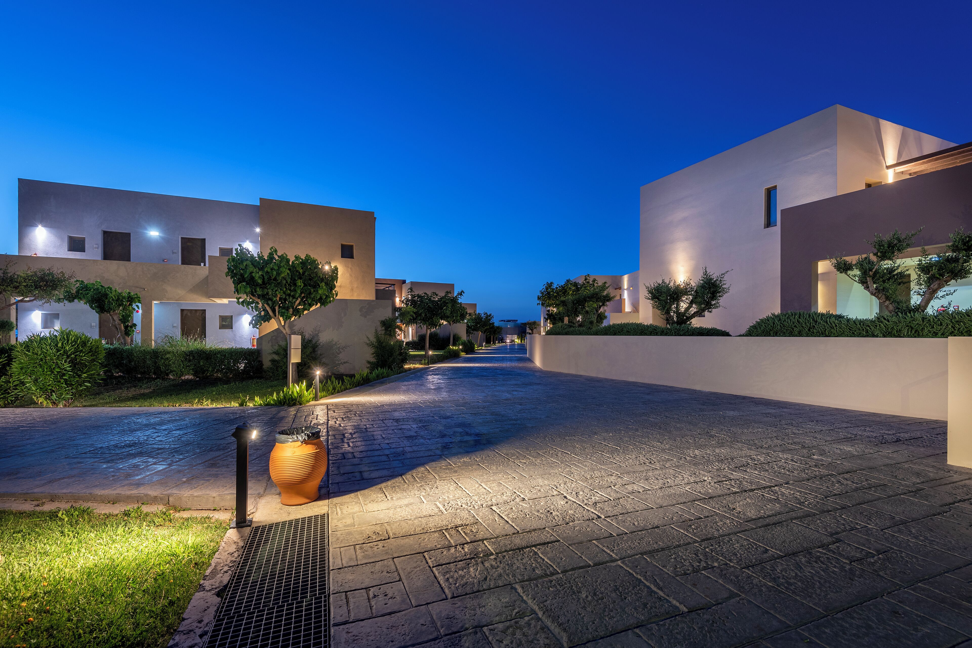 Un sendero pavimentado bordeado por edificios modernos con ventanas iluminadas, que se extiende hacia el horizonte.