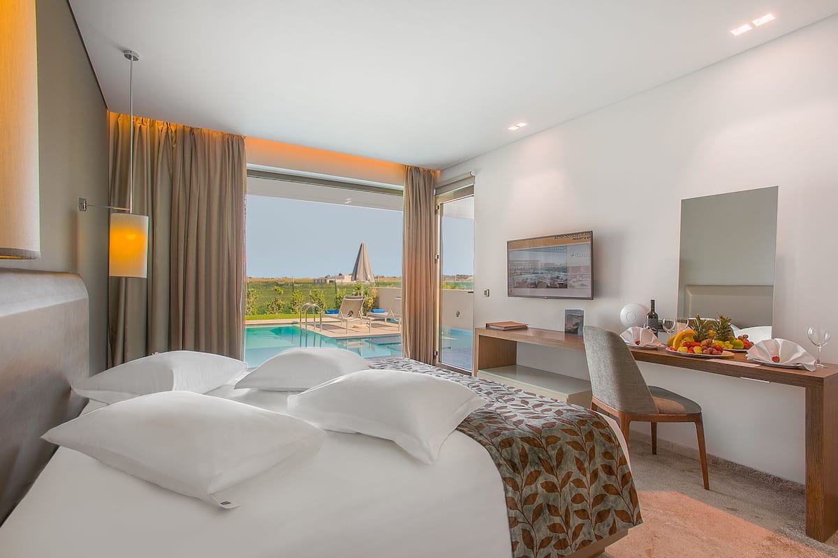 A hotel room with a bed, desk, and a view of a swimming pool and landscape.