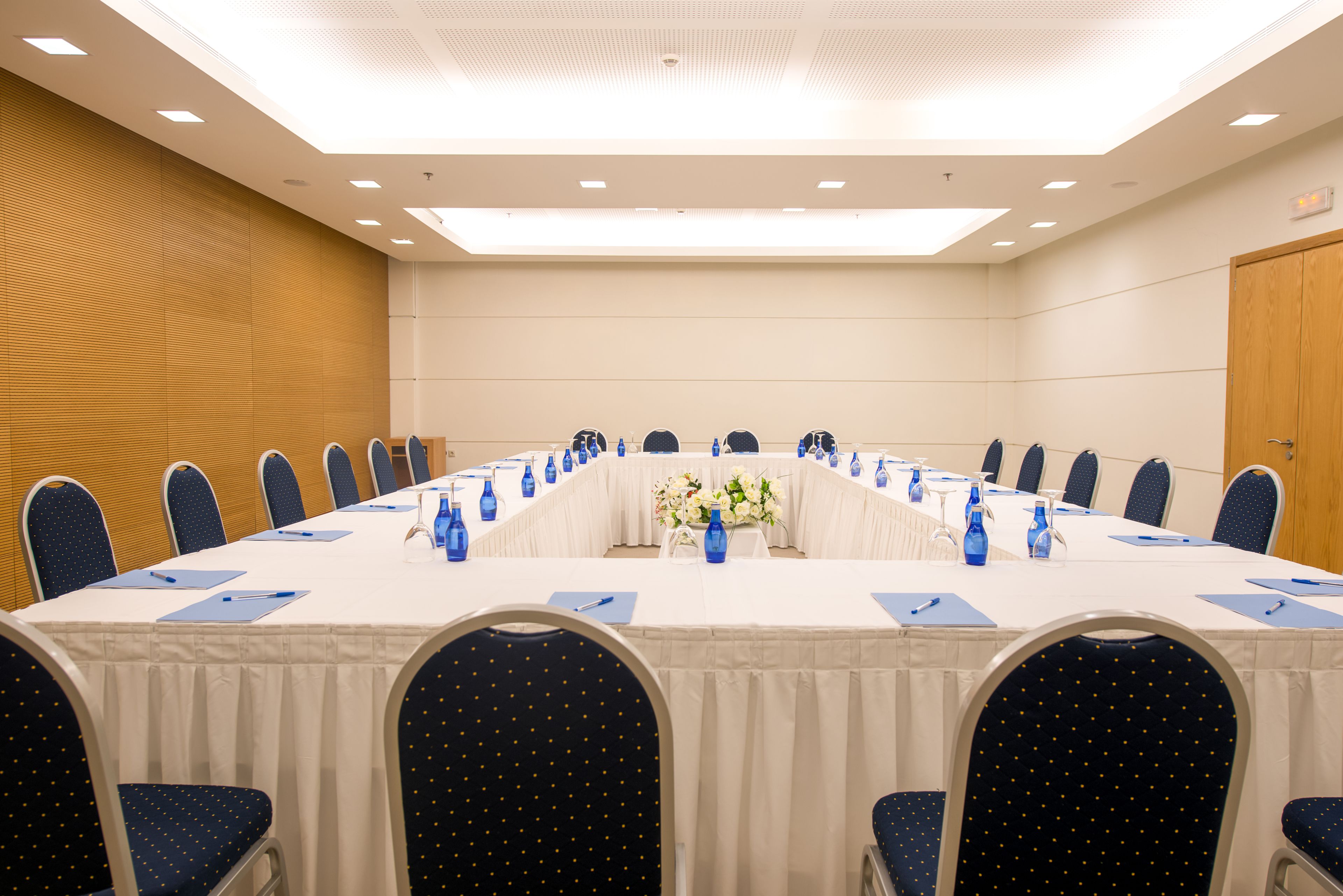 Una sala conferenze con un lungo tavolo, sedie e un centrotavola floreale.