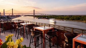 Eine Uferterrasse mit Außenplätzen, Blick auf eine Brücke und ein Boot auf dem Wasser.