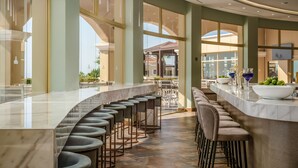 A modern bar area with a curved marble countertop, multiple bar stools, and a view of the outdoor patio area. - Lindos Imperial Resort & Spa (Rhodes)