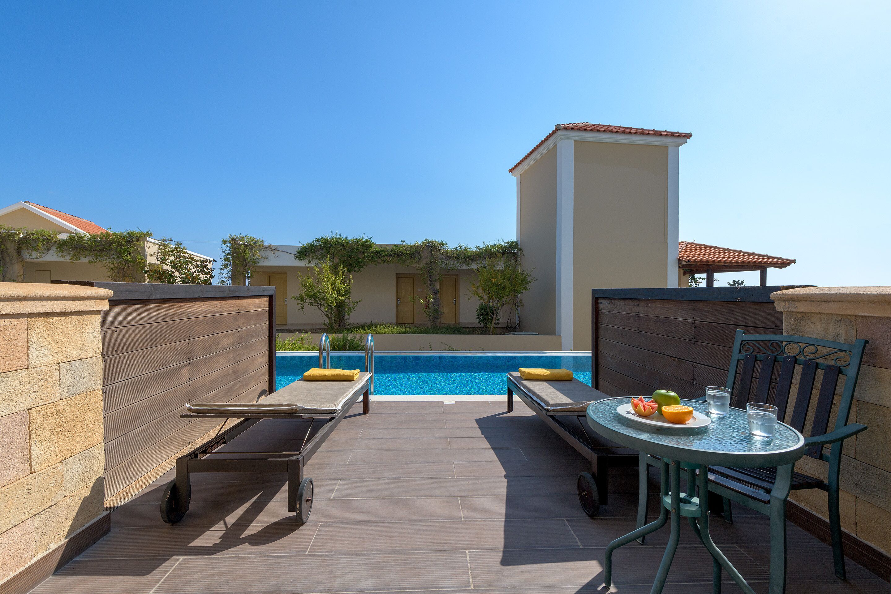 A rooftop pool area with lounge chairs, a table with a fruit plate, and a clear view of the pool.
