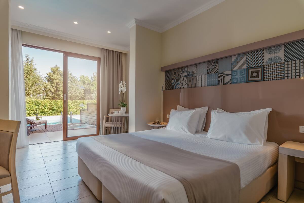 A hotel room with a large bed, a desk, a chair, and a view of an outdoor pool area.