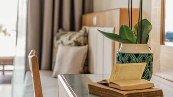 A modern living room with a glass coffee table, a wooden chair, a potted plant, and a bookshelf with books.