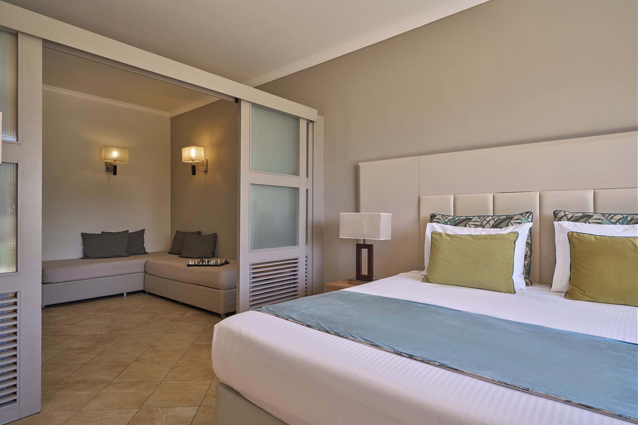 Habitación de hotel con una cama grande, un sofá, una mesita y dos lámparas de pared.