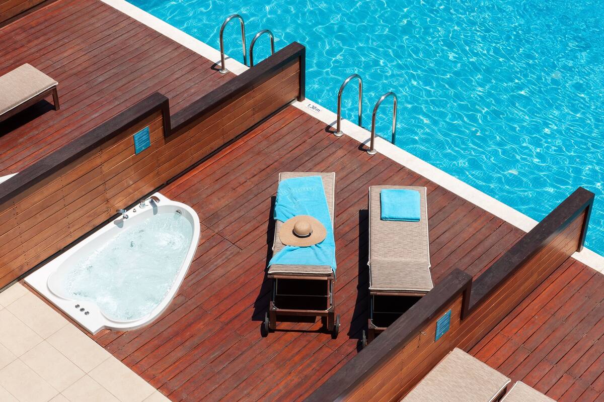 A wooden deck with a hot tub, lounge chairs, and a pool.