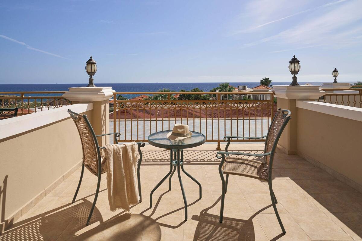 A balcony with a table and chairs, overlooking a coastal view.