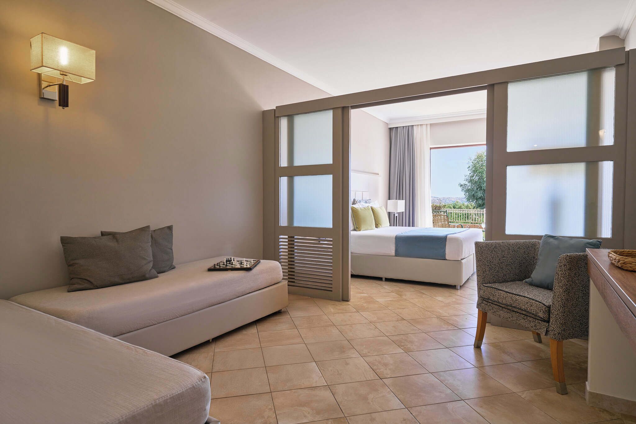 A modern hotel room with a sofa, a chair, a bed, and a balcony with a view.