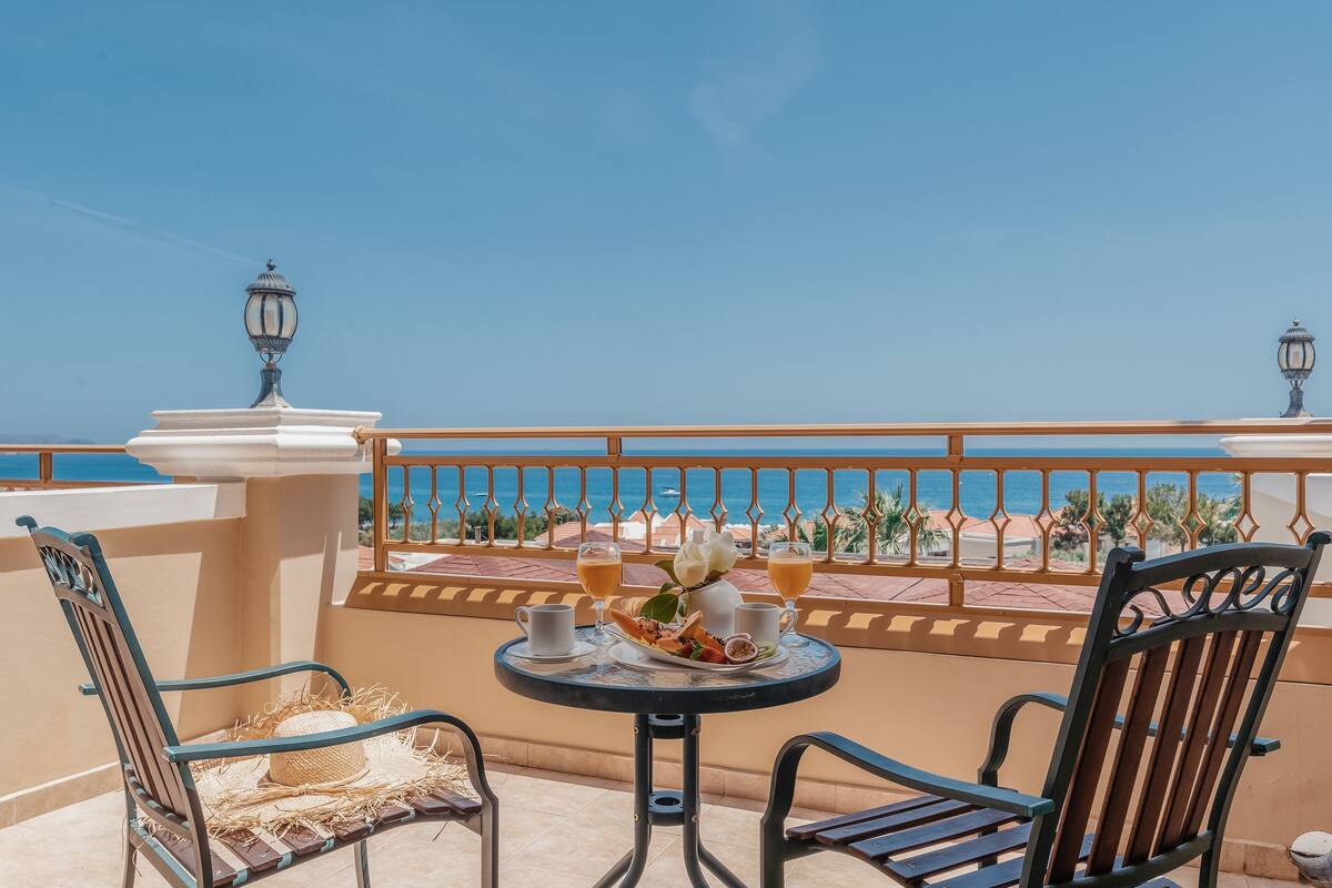 A balcony with a table set for two, featuring a plate of food, two cups, and a vase with flowers.