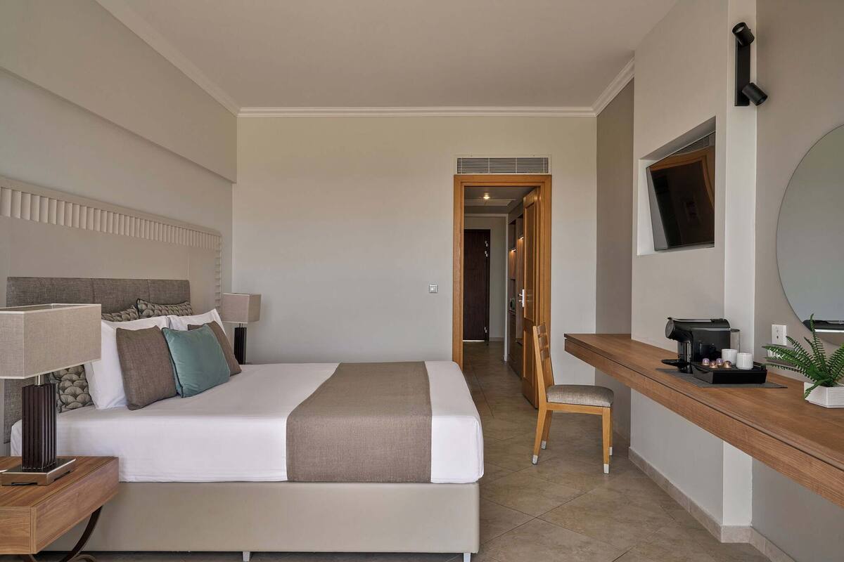 A hotel room with a bed, bedside table, lamp, and a desk with a coffee maker.