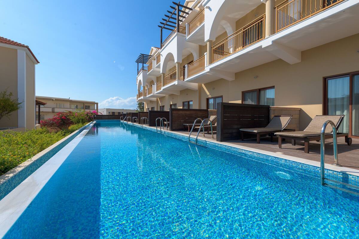 A swimming pool with lounge chairs and a building with balconies.
