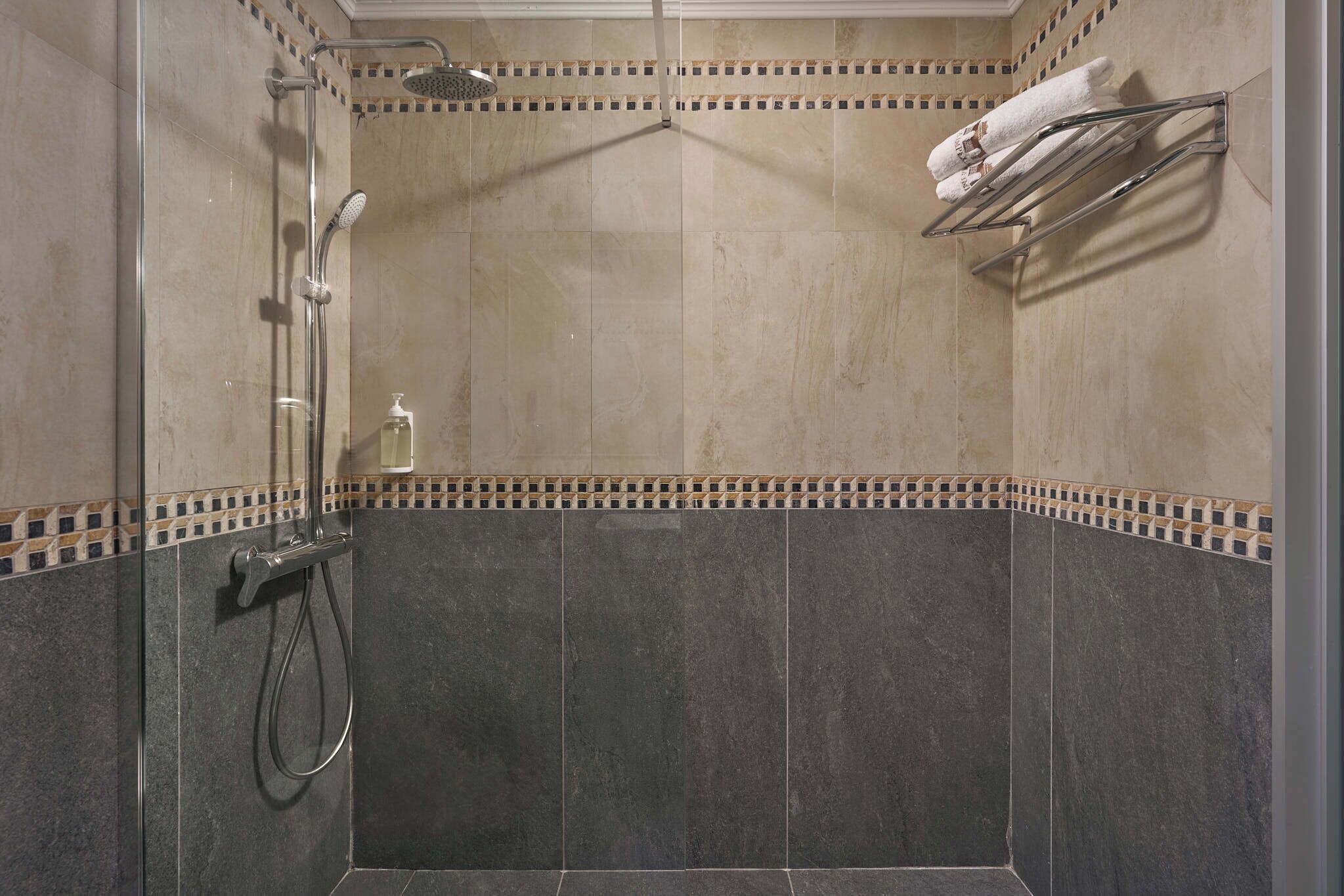 Douche met een glazen deur, een handdoekhouder met handdoeken en een zeepdispenser.