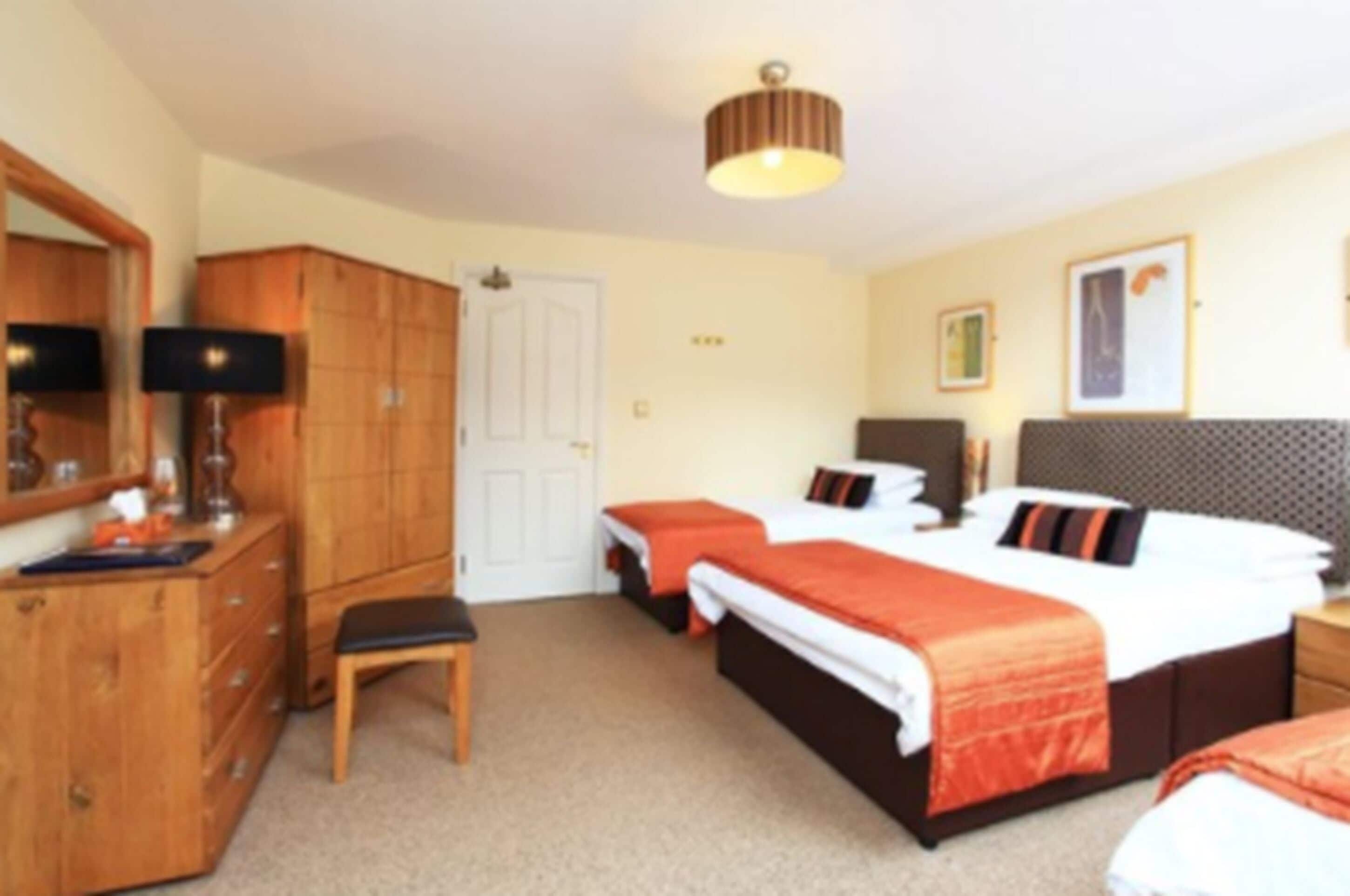 A hotel room with two beds, a wooden dresser, a bench, and a ceiling light.