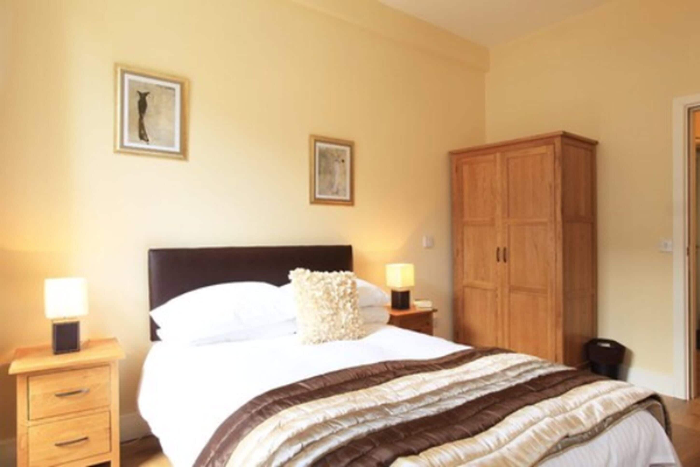 Un dormitorio con cama, mesitas de noche, un armario y dos cuadros en la pared.