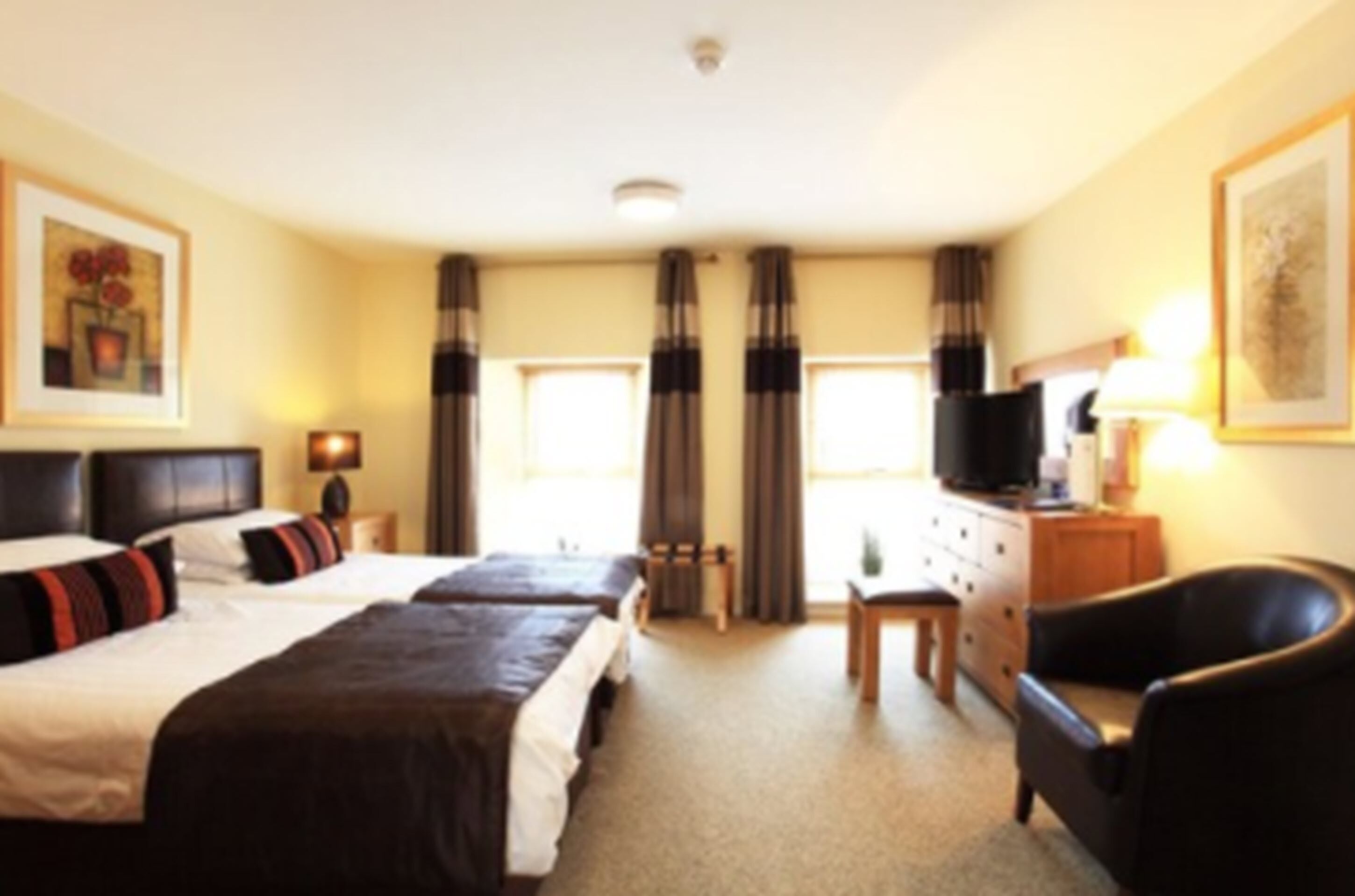 A hotel room with two beds, a desk, a chair, a television, and a window with curtains.