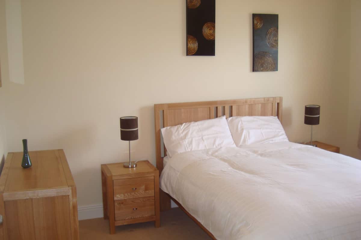Een slaapkamer met een houten bed, twee nachtkastjes, een nachtkast en twee wandlampen.