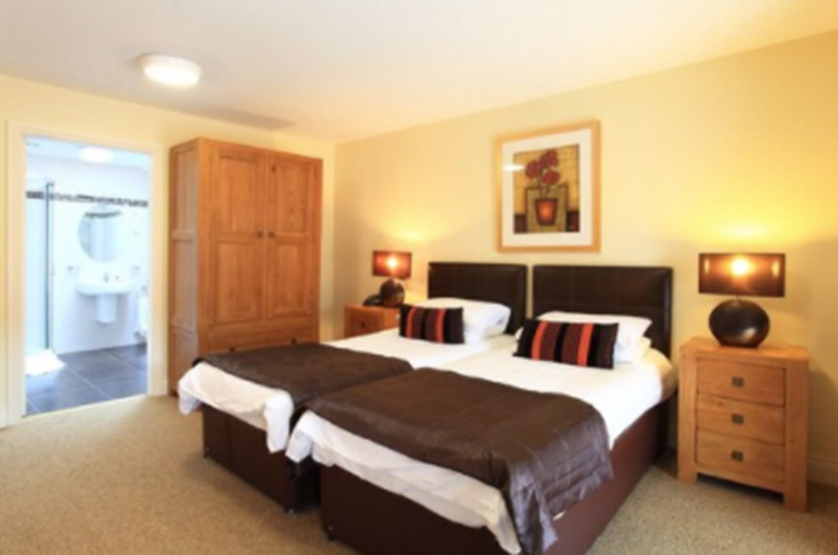 A double bed with a wooden headboard, two bedside tables with lamps, a framed picture on the wall, and a wooden wardrobe.