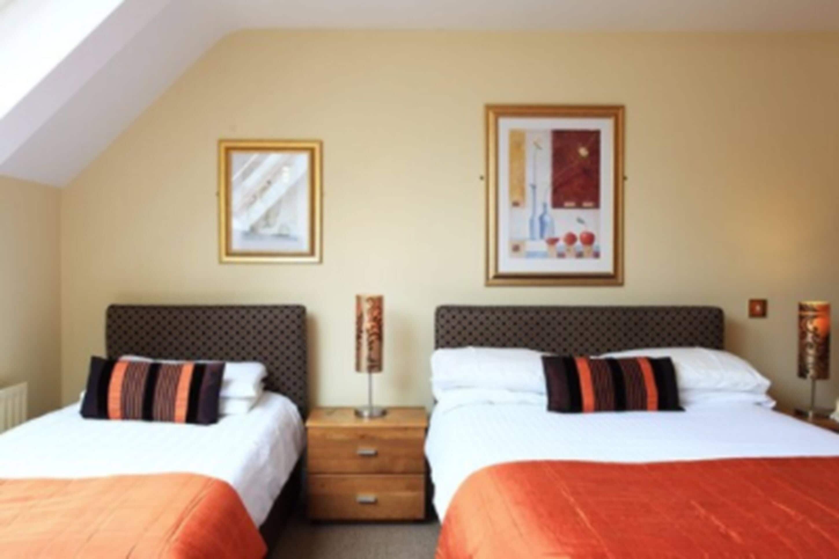 Une chambre d’hôtel avec deux lits, une table de chevet en bois et deux œuvres d’art encadrées accrochées au mur.