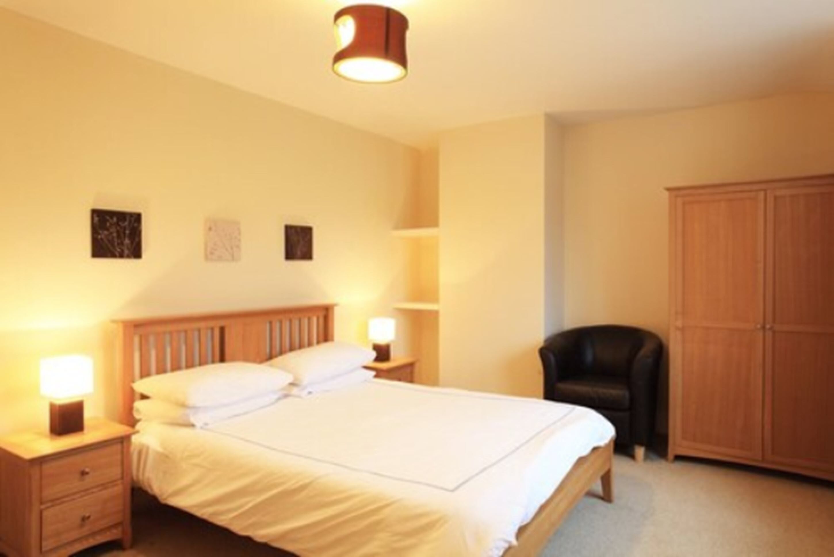 Een slaapkamer met een enkel bed, nachtkastjes met lampen, een stoel en een kledingkast.