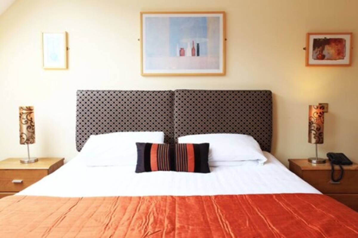 Een hotelkamer met een groot bed, een kamerhoge bekleding op het hoofdeinde, twee nachtkastjes en ingelijste foto's aan de wand.