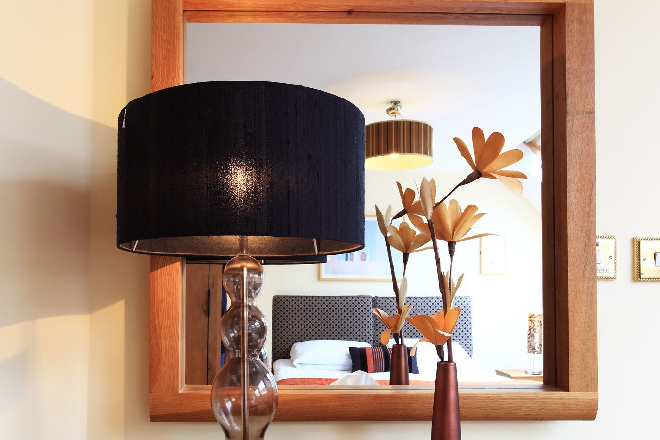 Une pièce comprenant un lit, un miroir, une lampe et un vase décoratif contenant des branches.