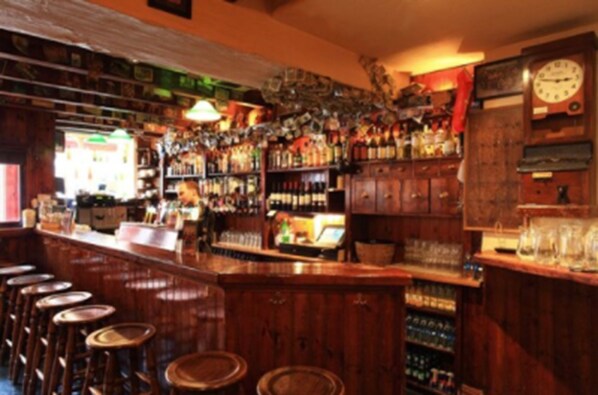 Un bar con taburetes de madera, estanterías llenas de botellas y un reloj en la pared.