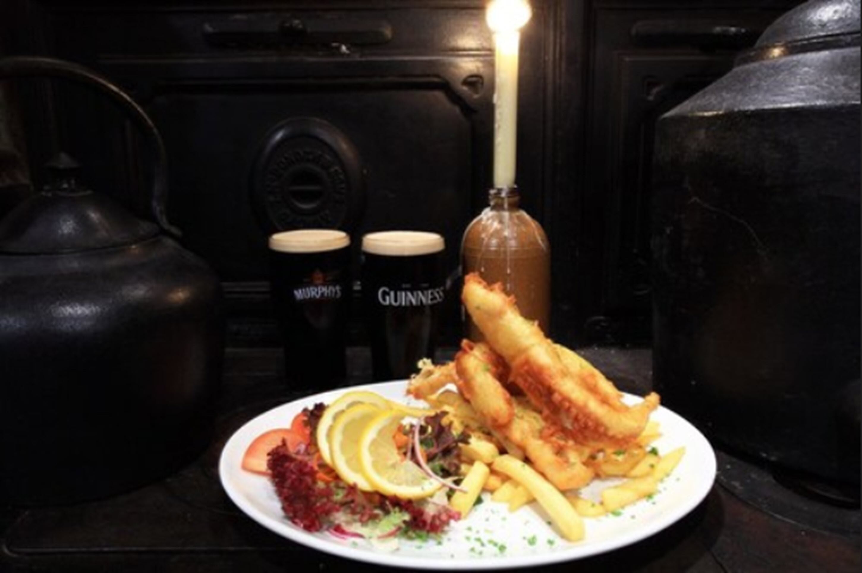 Une assiette de poisson-frites accompagnée d’une salade et de frites, le tout servi avec deux bouteilles de bière.