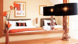 Hotellihuone, jossa on suuri sänky, puinen pääty, yöpöytä lampun kanssa ja peili, joka heijastaa huonetta.
