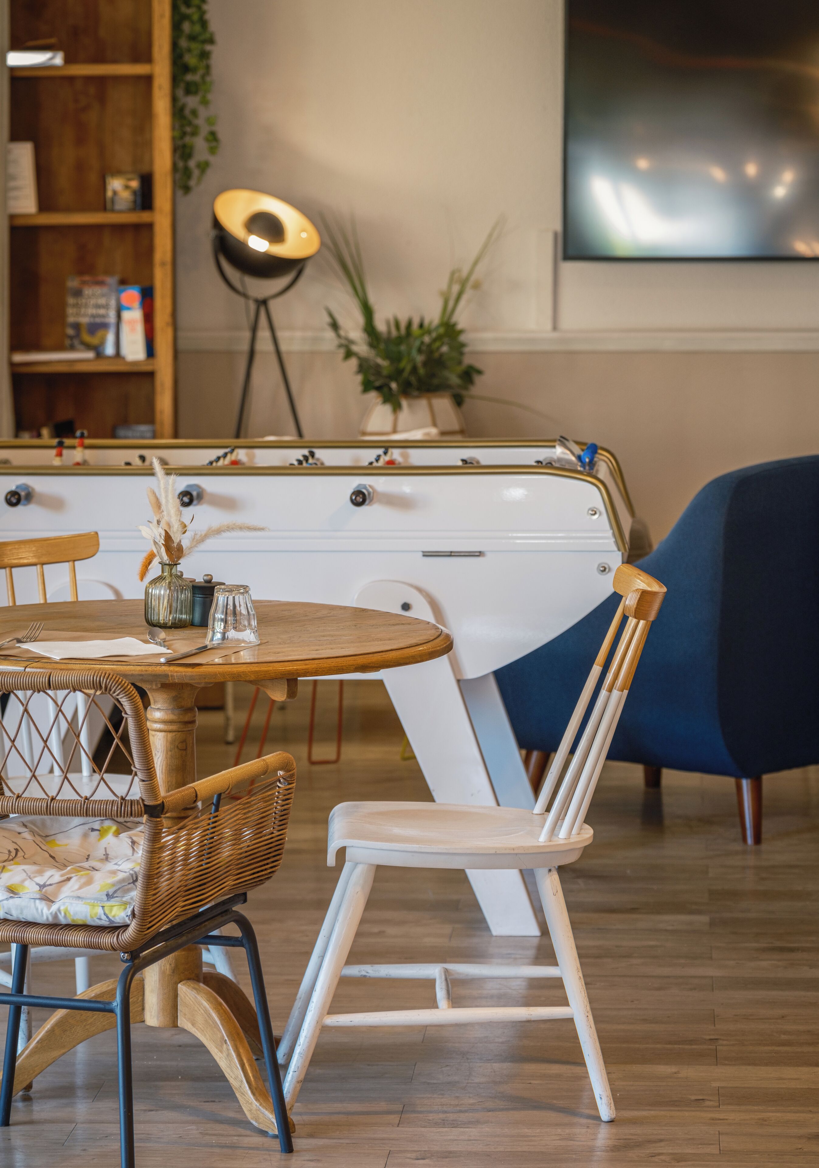 A dining area with a round wooden table, wicker chairs, a white chair, a vintage-style refrigerator, and a blue armchair.