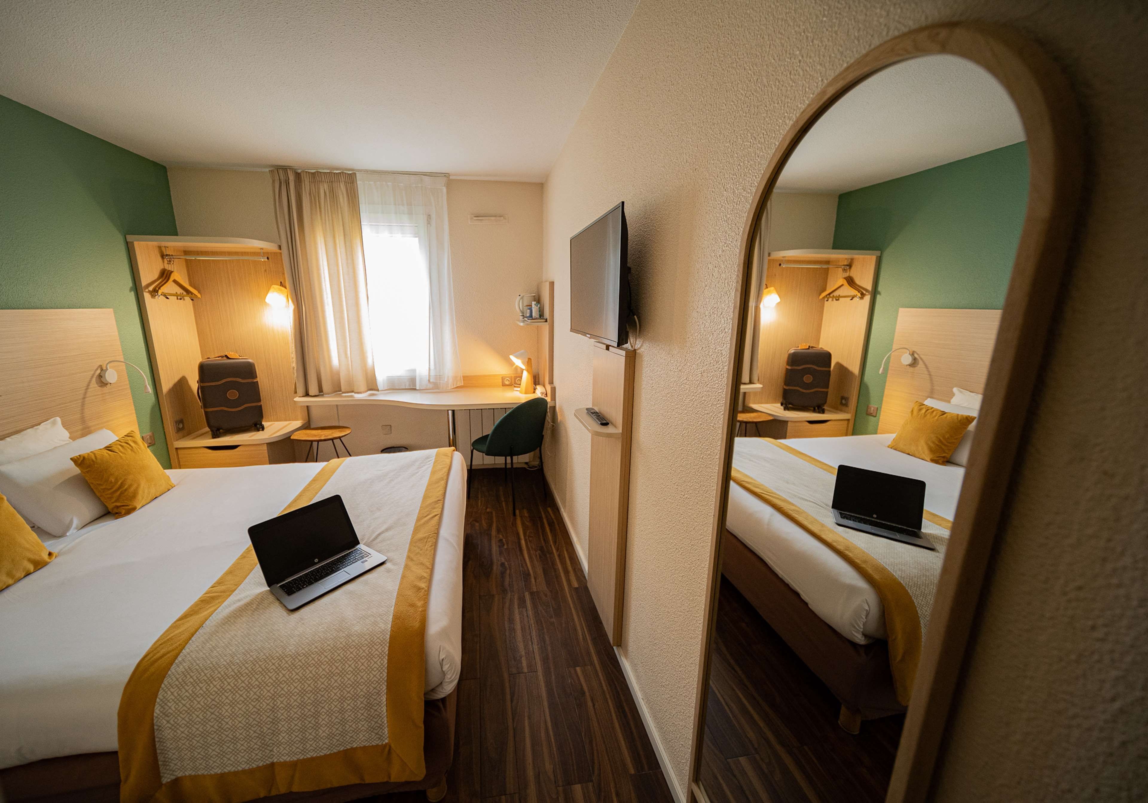 A hotel room with two beds, a desk, a chair, a TV, and a mirror.