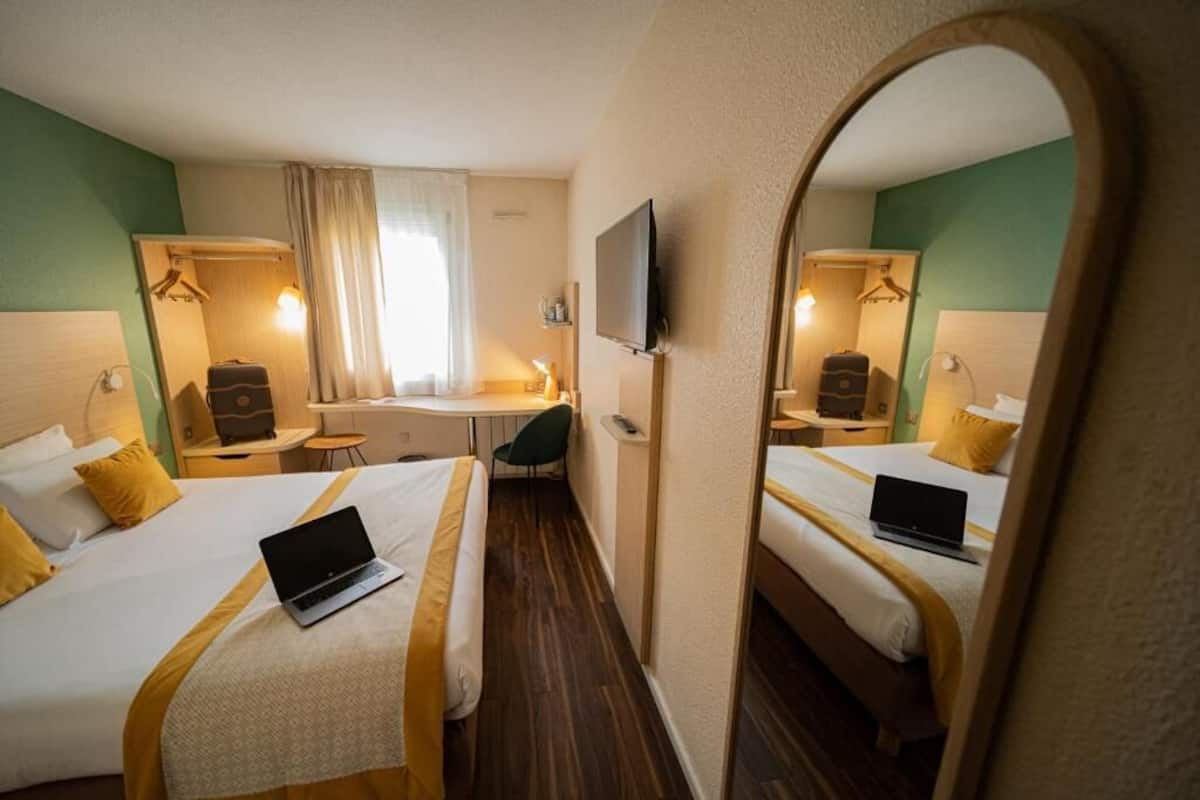 Une chambre d’hôtel avec deux lits, un bureau, une chaise, une télévision et un miroir.
