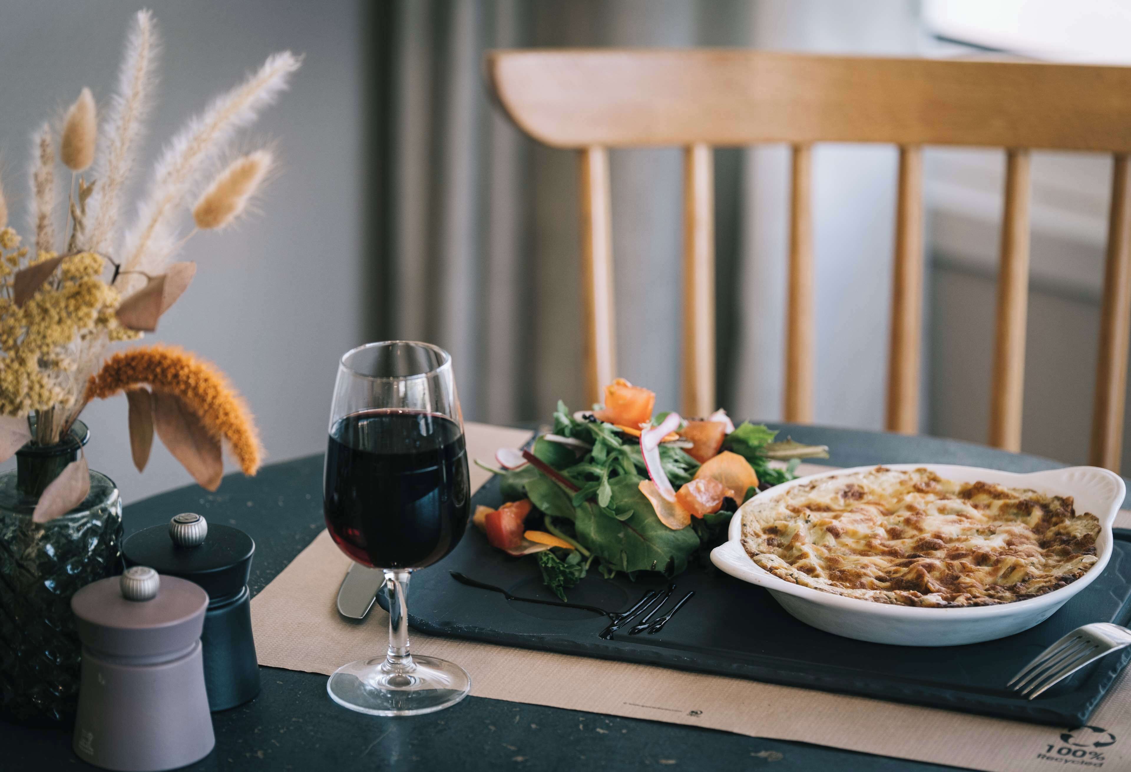 Una mesa de comedor con una copa de vino tinto, una ensalada y un plato al horno.