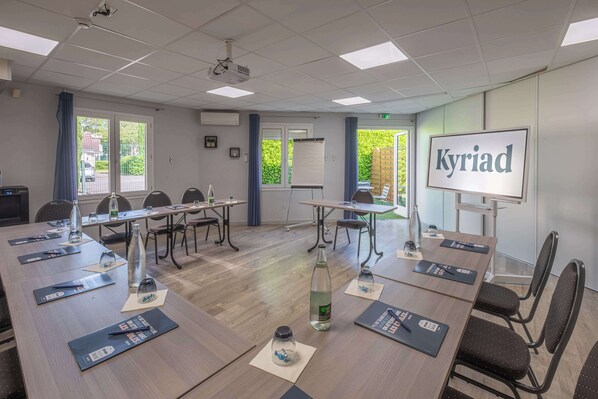 Ein Konferenzraum mit Projektor, Präsentationsleinwand und Tischen mit Wasserflaschen und Notizblöcken.