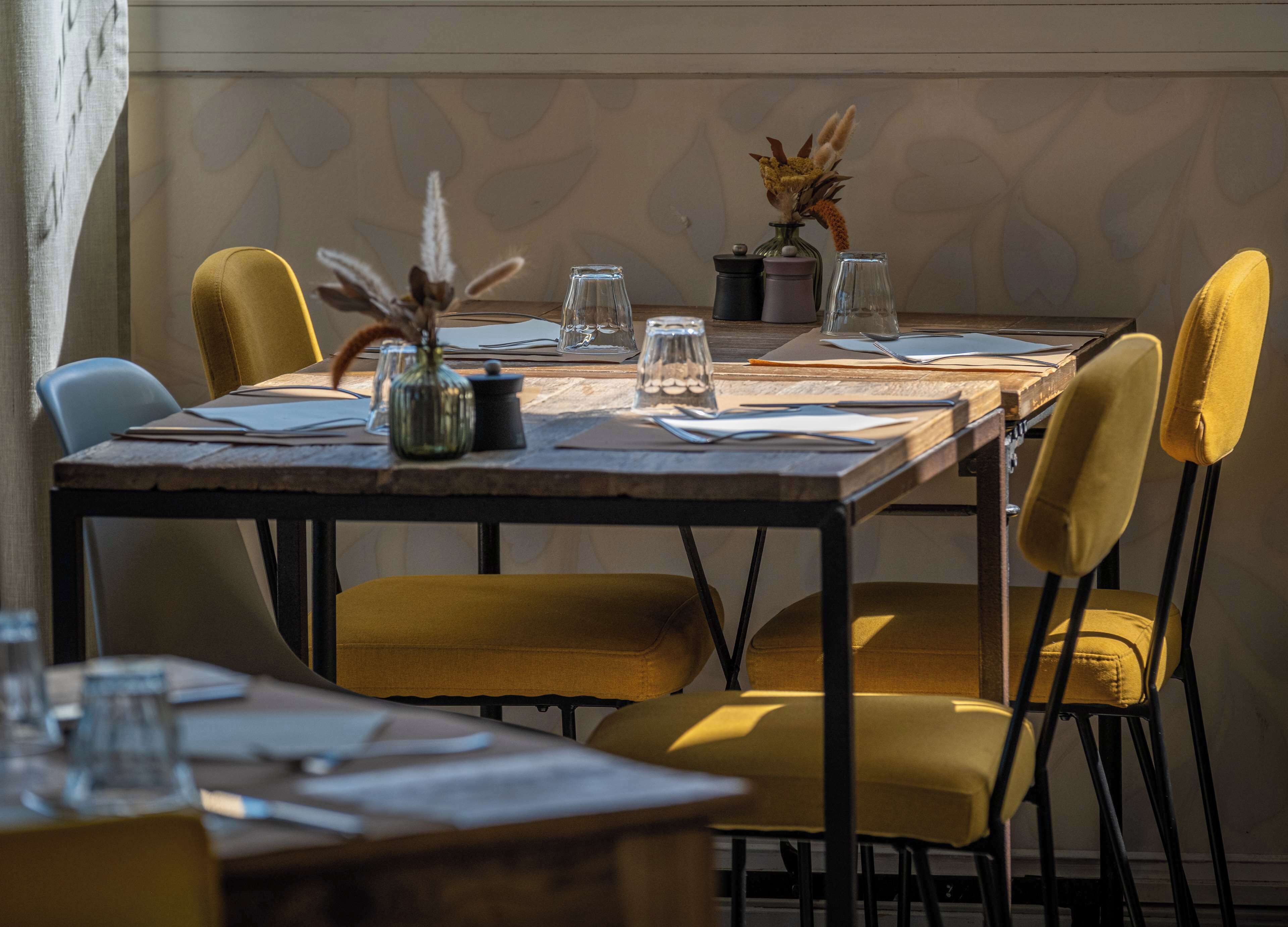 Una mesa de comedor con sillas amarillas, vasos transparentes y un jarrón decorativo.