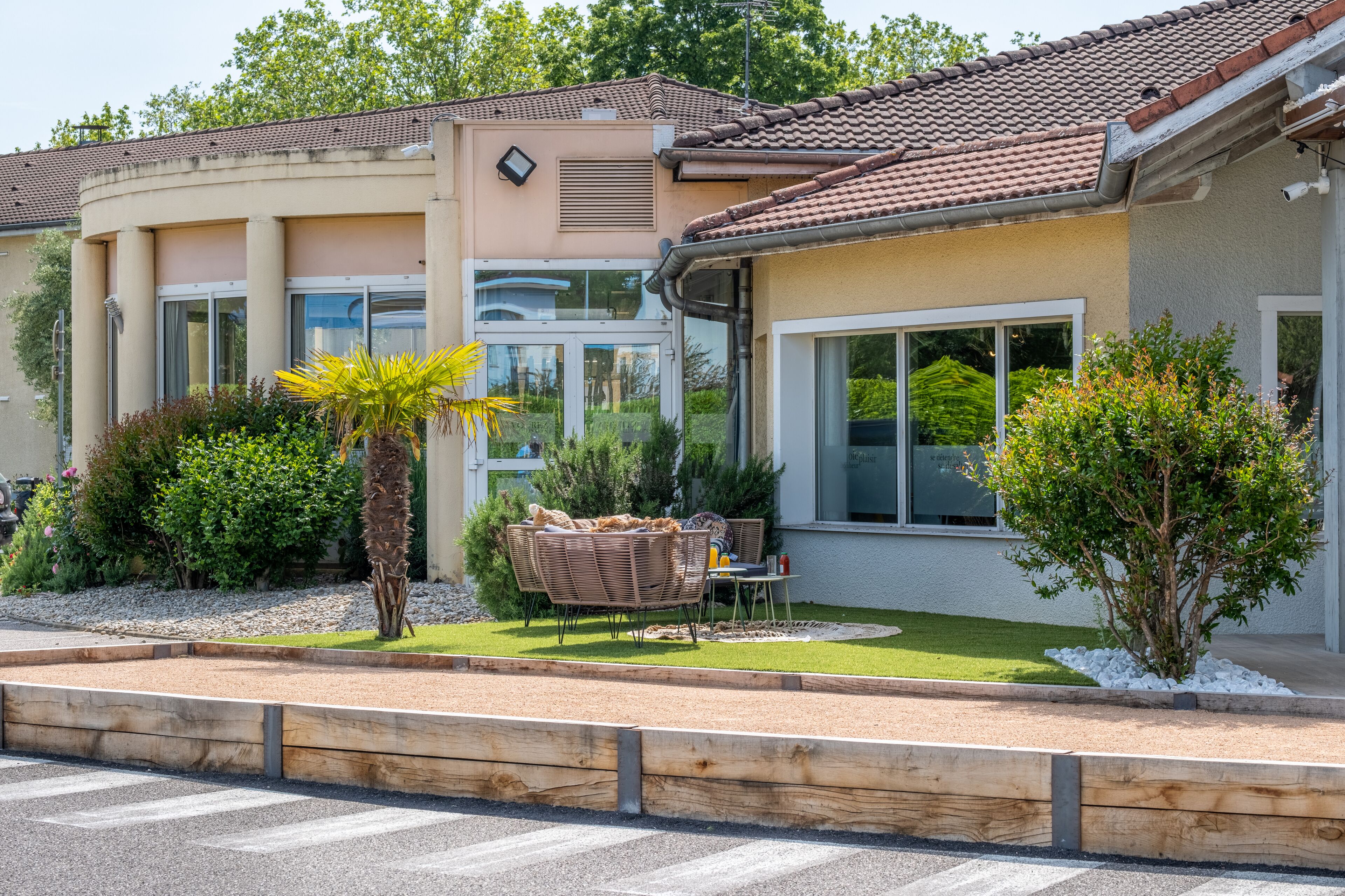 Un edificio residencial con fachada curva, amplios ventanales y un jardín bien cuidado con zona de patio.