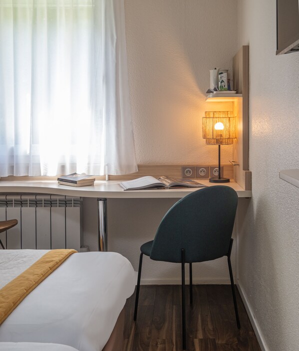 Une chambre d’hôtel avec un lit, un bureau avec une chaise, une lampe et un radiateur.