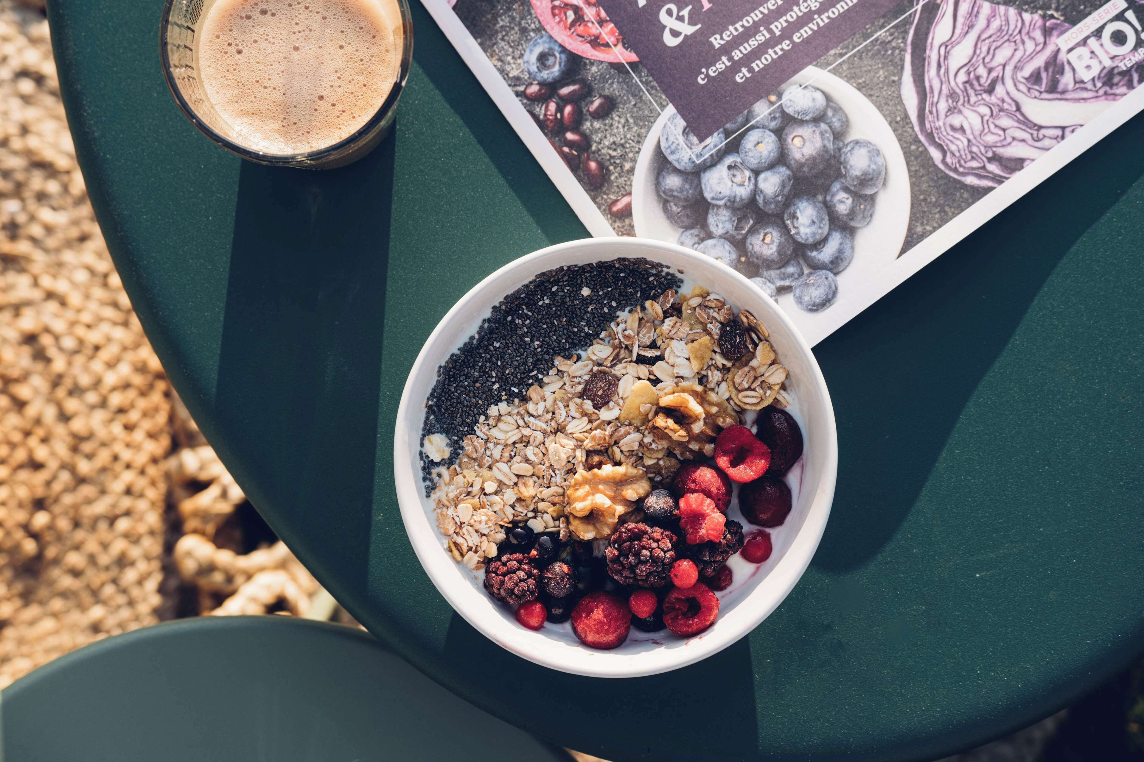 A bowl of granola with berries and a glass of coffee on a table.