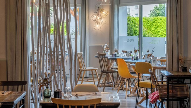 Un restaurante con mobiliario de madera, una mampara de vidrio y lámparas colgantes.